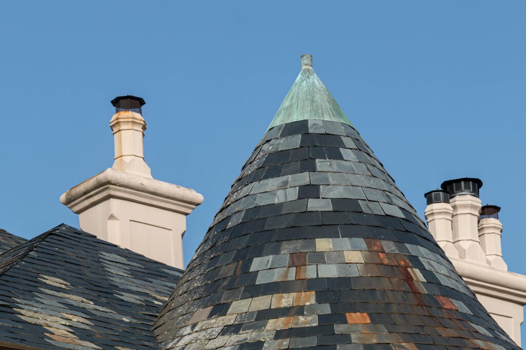 pexels photo 15979049 15979049 Close-up of a residential building's chimney and copper-topped tiled roof against a clear blue sky.