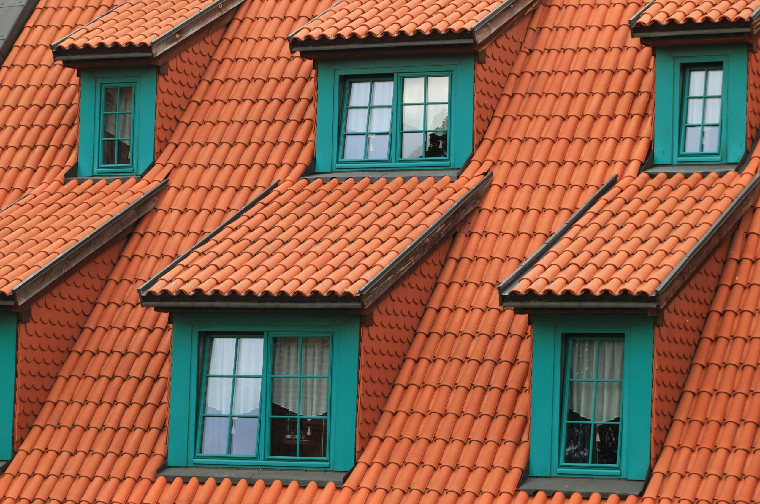About US Close-up of an orange tiled roof with green framed dormer windows, creating a colorful architectural contrast.