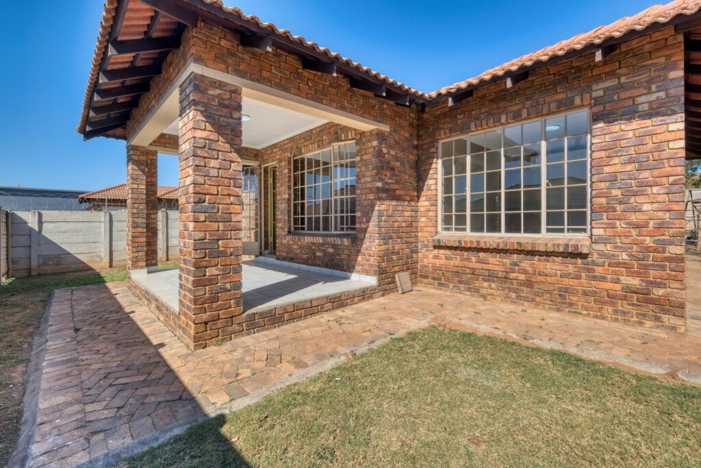 pexels photo 26984990 26984990 A red brick house featuring large windows and a sunlit porch, ideal for real estate listings.