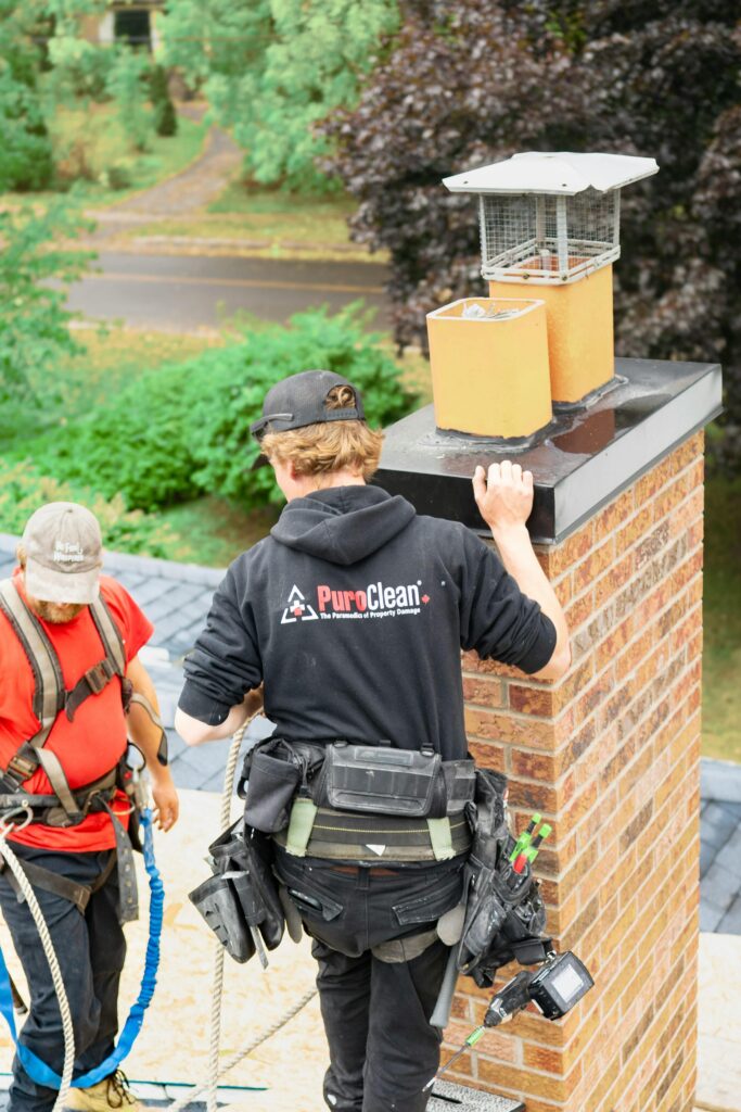 pexels photo 34020199 34020199 Two workers conducting a thorough chimney inspection on a rooftop in a wooded neighborhood.