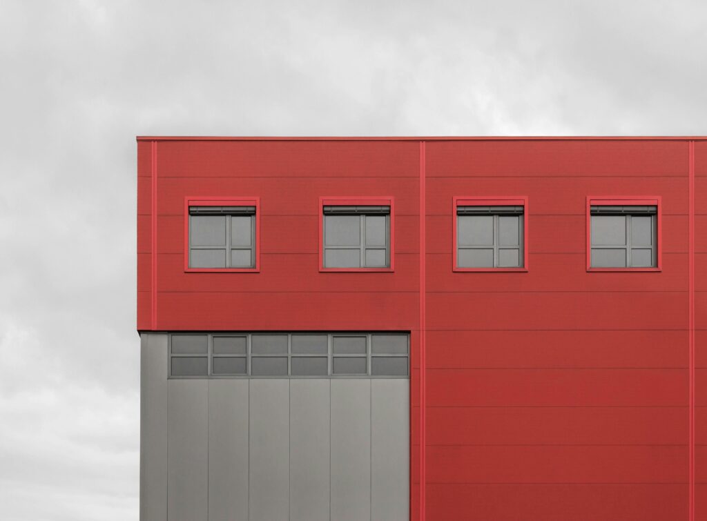 Minimalist red building exterior with black windows under a cloudy sky.